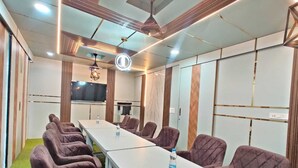 Un salón de conferencias con una larga mesa, varias sillas, un ventilador de techo y una pantalla de televisión.