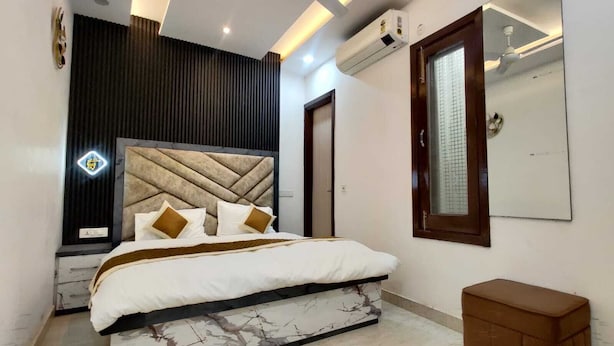 Un dormitorio moderno con una cama de mármol, un ventilador de techo, un equipo de aire acondicionado, un espejo grande y un pequeño banco de madera.
