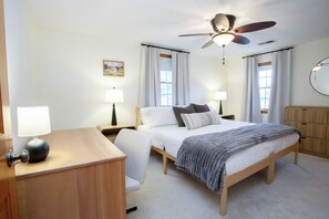 Una camera da letto con un letto, comodini, una scrivania, una ventola a soffitto e uno specchio.