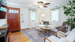 A living room with a wooden door, a ceiling fan, a sofa, a coffee table, and a plant. - Farmington gem near UConn Health with garage • Fast Wi-Fi • Dog Friendly (Farmington)