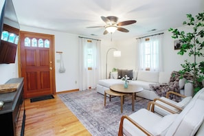 A living room with a wooden door, a ceiling fan, a sofa, a coffee table, and a plant. - New Stylish 2BR Garage Balcony Pet Friendly Fast WiFi (Farmington)