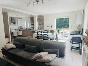 A modern living room with a grey sofa, a dining area with a white table and chairs, and a kitchen in the background. - Quiet Provencal escape - Ground floor villa 75m², pool & terrace (Saint-Paul-en-Forêt)