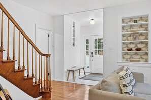 Una escalera con balaustres de madera, un banco, una zona de estar acolchada y un estante con adornos.