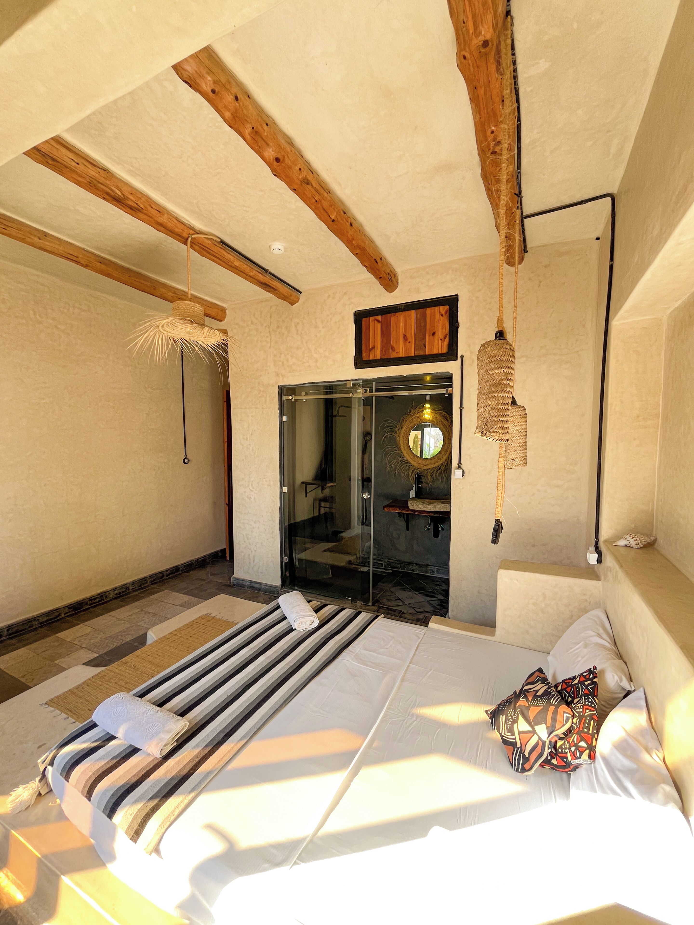 A bedroom with a bed, a window, a door, and a ceiling with exposed beams.