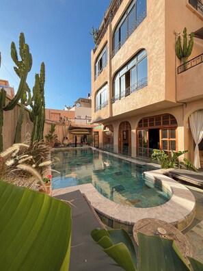 A pool area with a clear blue sky, a building with balconies, and cacti.