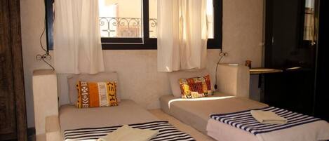 A room with two beds, a window with curtains, a door, and a view of buildings outside.
