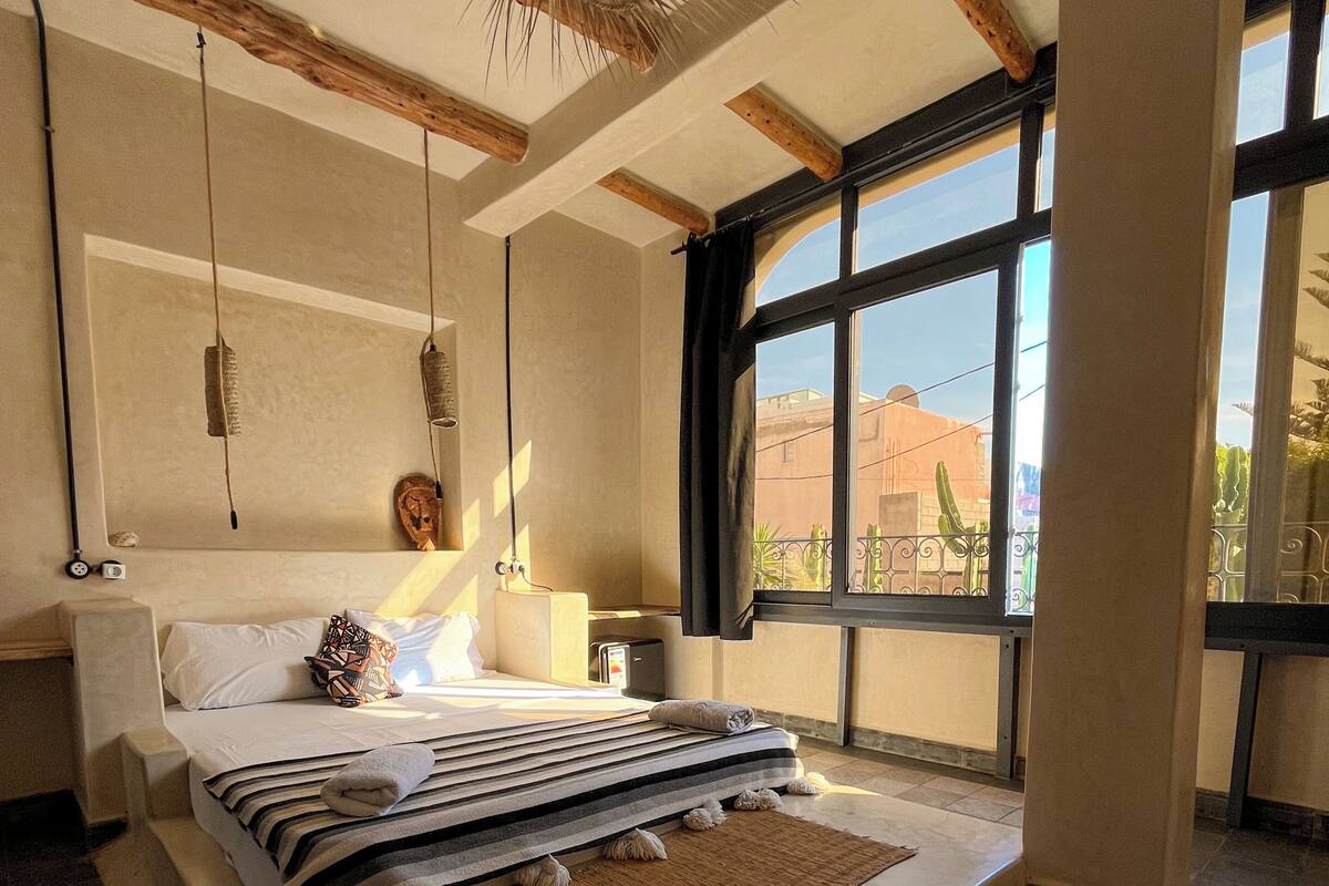 Een slaapkamer met een groot bed, een raam met uitzicht, een hanglamp en een houten plafond.