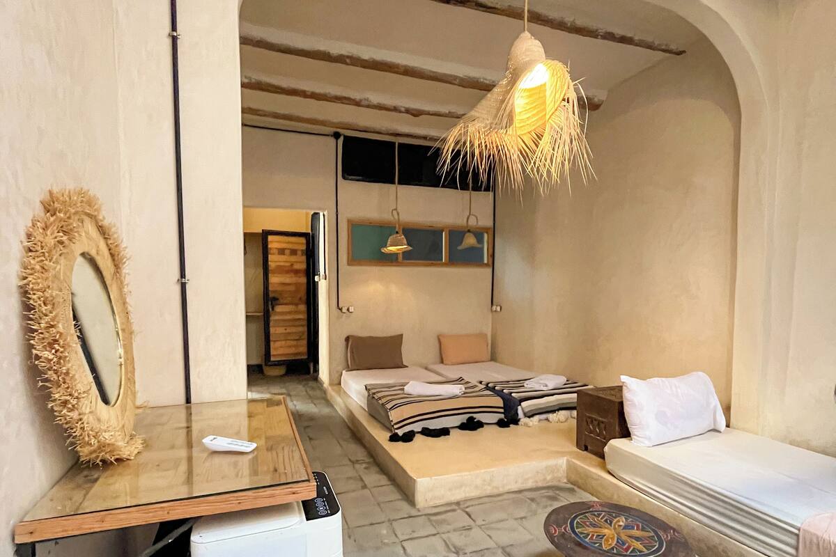 Een kleine hotelkamer met een bed, een tafeltje, een koelkast, een spiegel en een hanglamp.