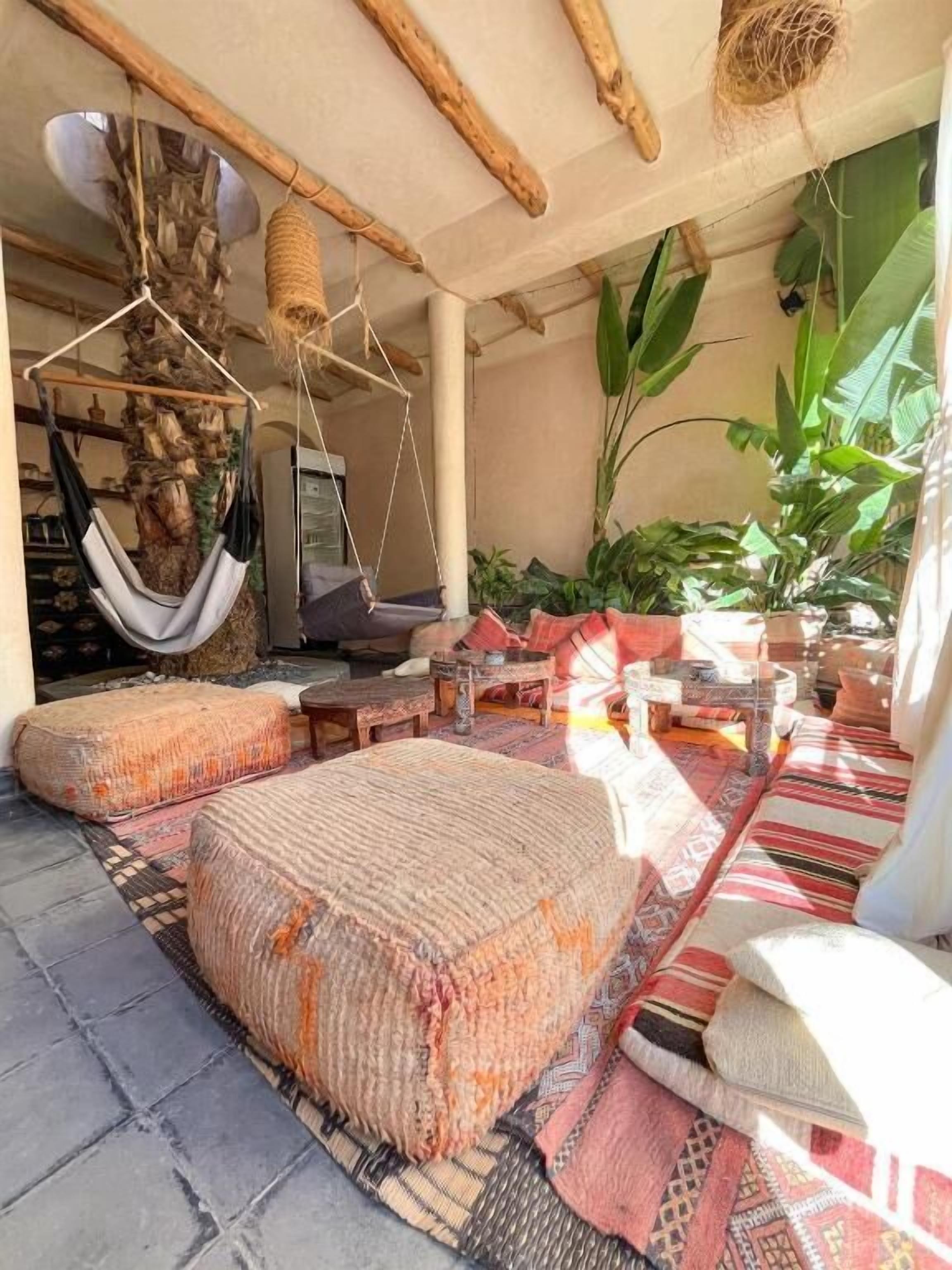 Un espace extérieur accueillant, aménagé avec des hamacs, des poufs en fibres tressées et un tapis à motifs.