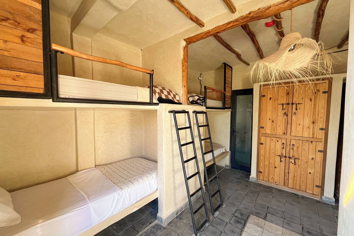 Een slaapkamer met stapelbedden, een houten plafond, een deur en een gevlochten mand die aan het plafond hangt.