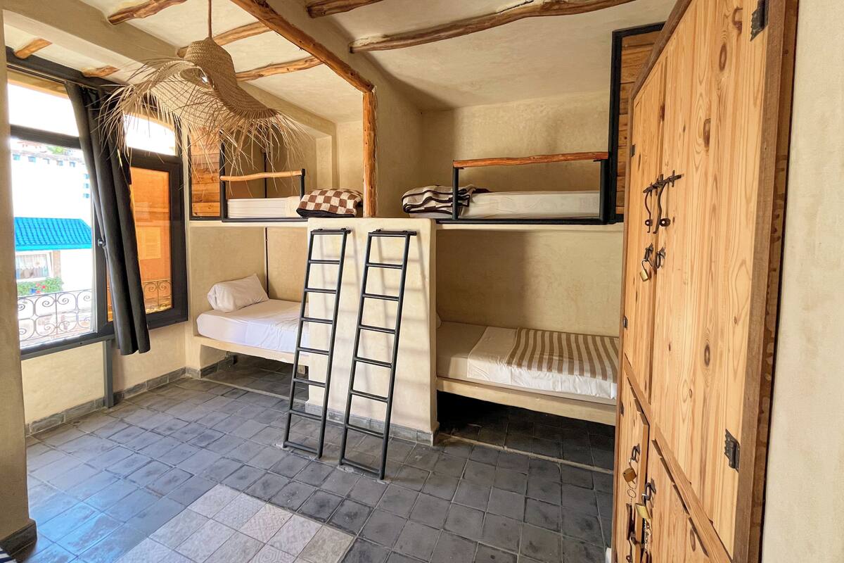 Een kleine kamer met stapelbedden, een houten garderobe en een raam met uitzicht.