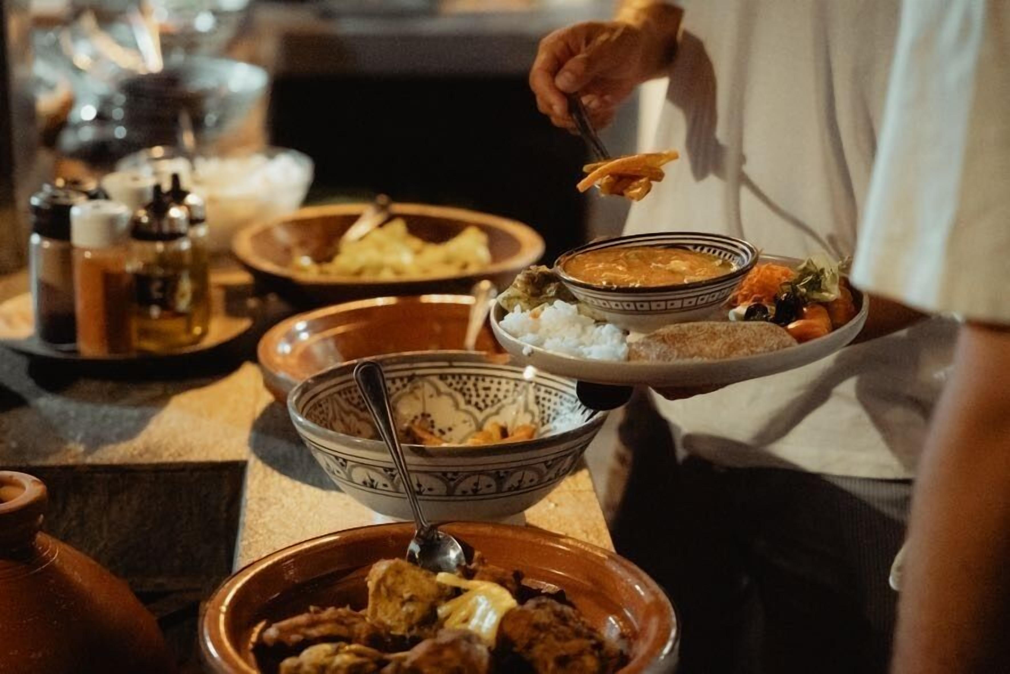 Una persona sirve comida de una bandeja con varios platos, entre ellos, arroz, sopa y un guiso de carne.