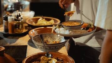 Una persona sirve comida de una bandeja con varios platos, entre ellos, arroz, sopa y un guiso de carne.
