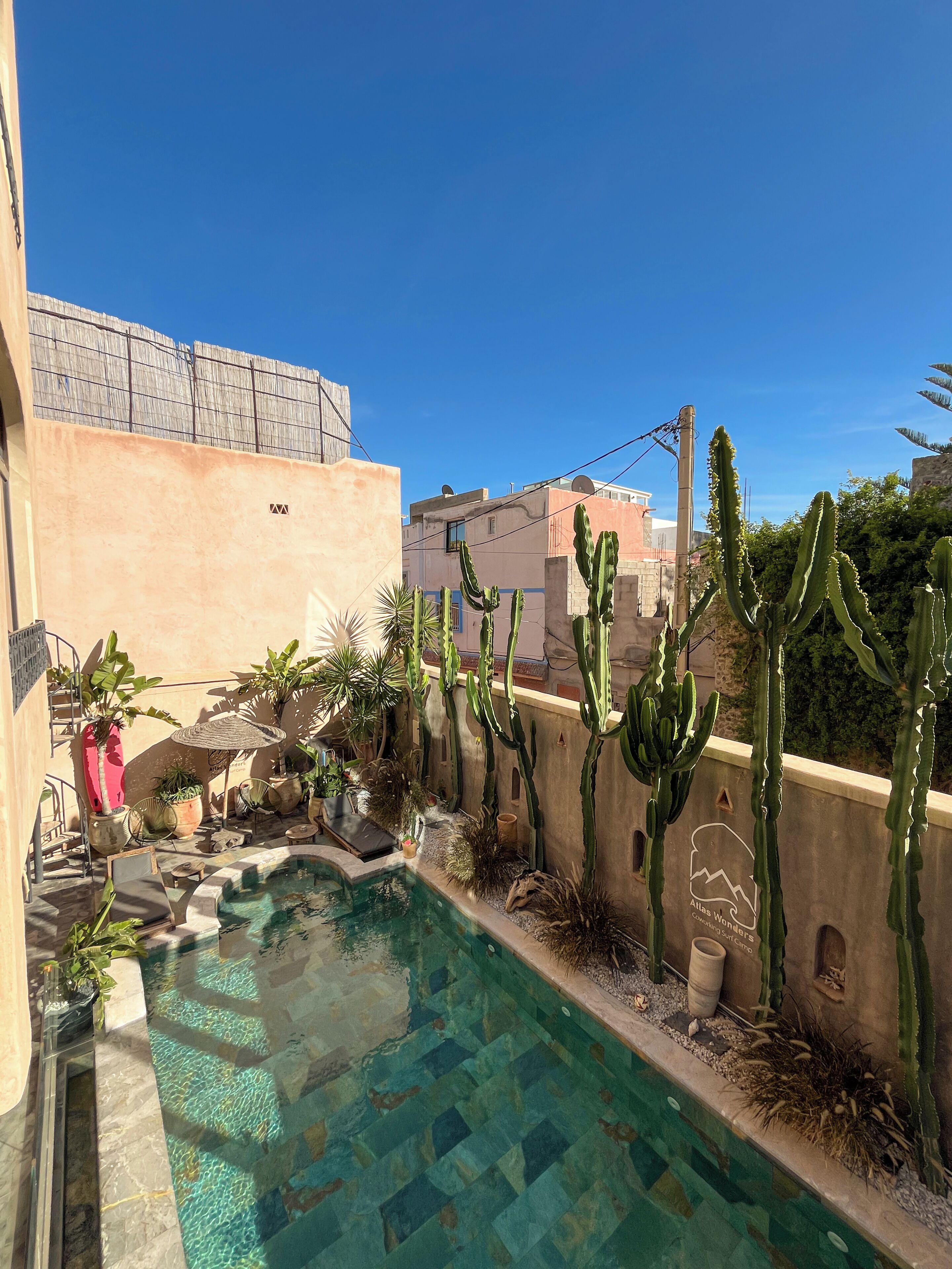 Un espace piscine agrémenté de cactus, un petit coin salon et une vue sur les bâtiments en arrière-plan.