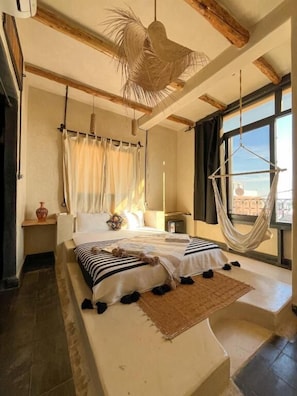 A bedroom with a bed, a hanging chair, a window, and a view. - RIAD ATLAS SURF (Tamraght)