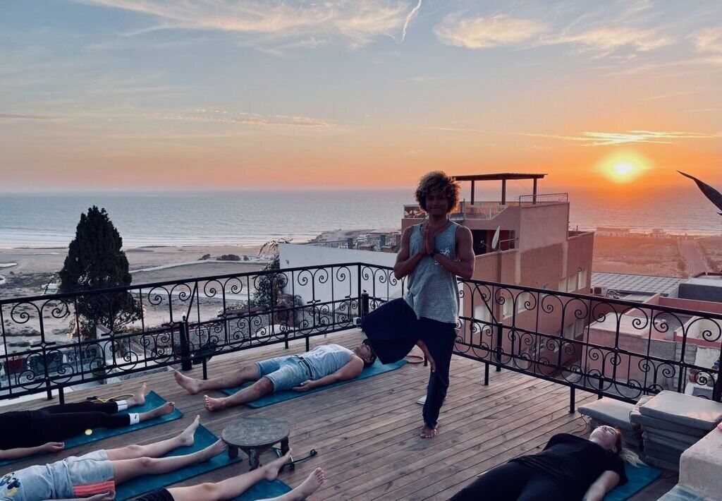 Clase de yoga en una terraza de madera con vista al océano al atardecer.