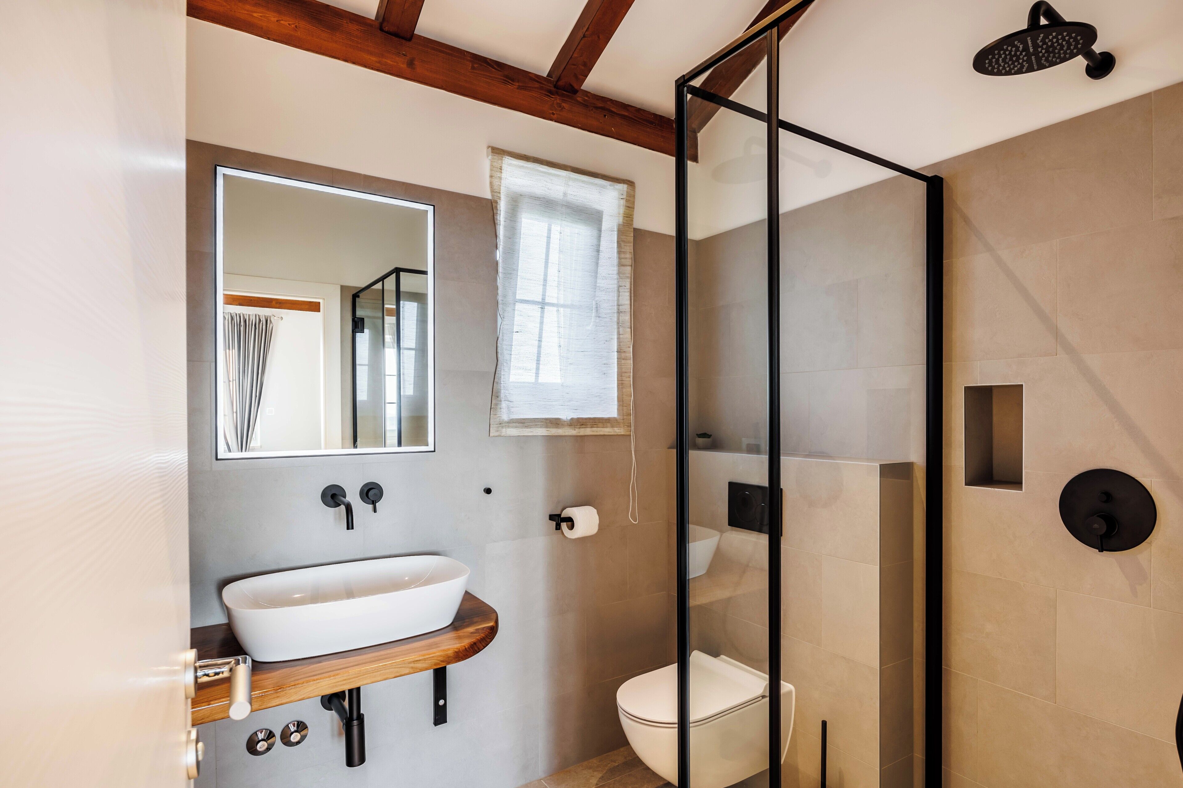 A bathroom with a wooden vanity, a large mirror, a toilet, and a glass-enclosed shower area.