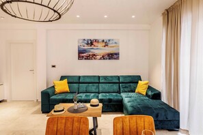 Ein modernes Wohnzimmer mit einem grünen Modulsessel, einem Holztisch und einem Gemälde an der Wand.