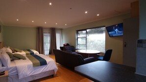 A hotel room with a bed, a sofa, a small table, a TV, and a window with blinds.