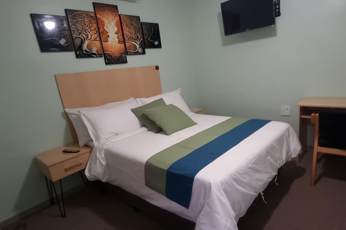 Una camera d'albergo con un letto, un comodino e una piccola scrivania.
