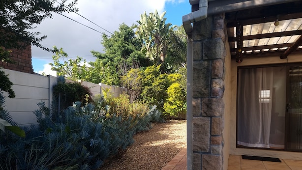A patio area with a stone wall, a gravel path, and various plants.