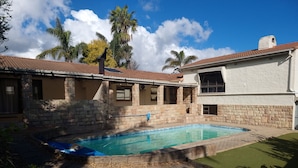 A swimming pool with stone walls, a covered patio, and a clear blue sky.