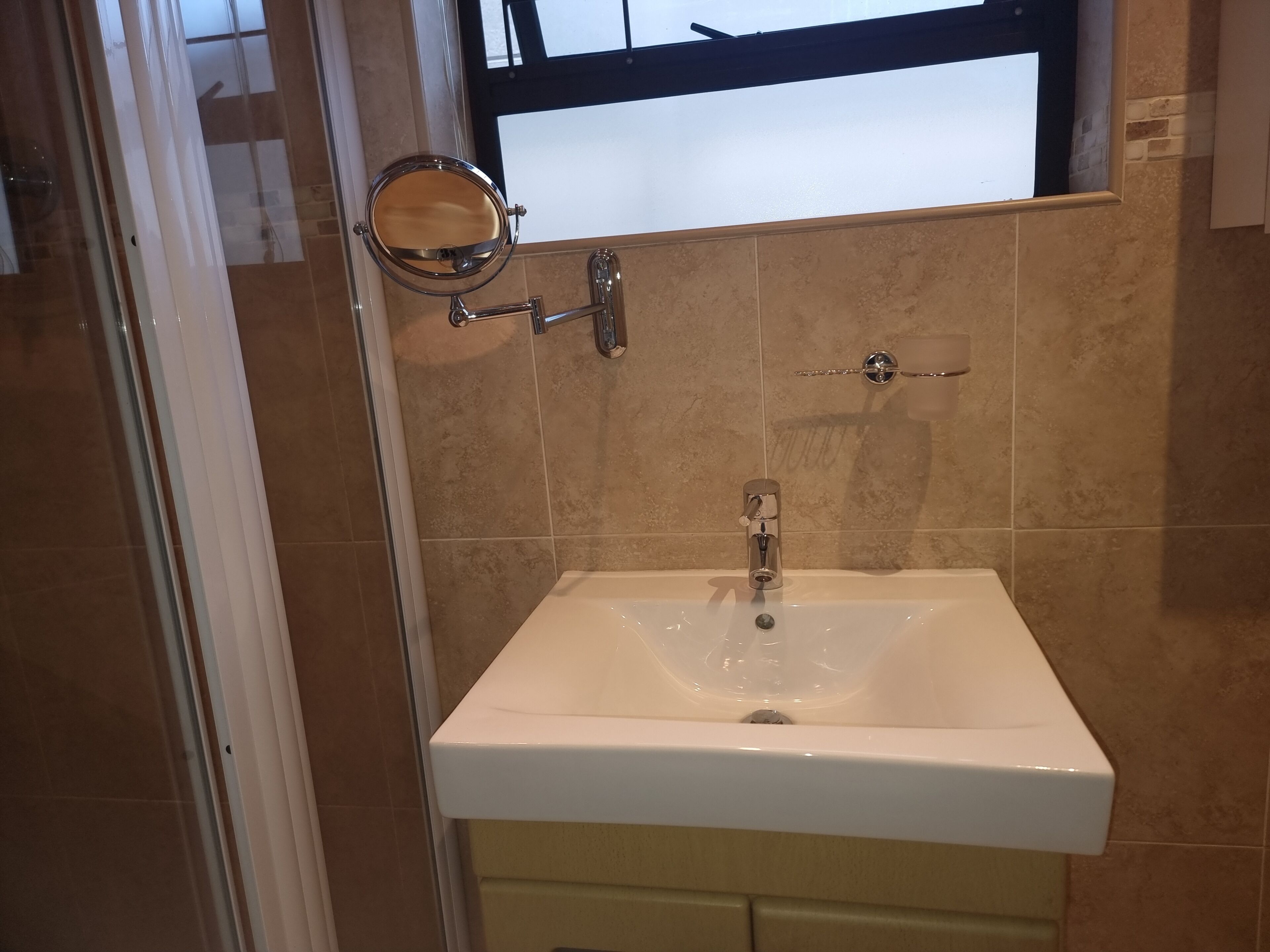 Un bagno con un lavandino bianco, uno specchio e una finestra sopra al lavandino.