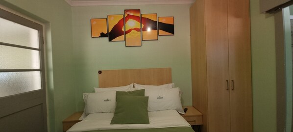 Une chambre à coucher comprenant un lit, des tables de chevet, une armoire en bois et un mur orné d’œuvres d’art abstraites.