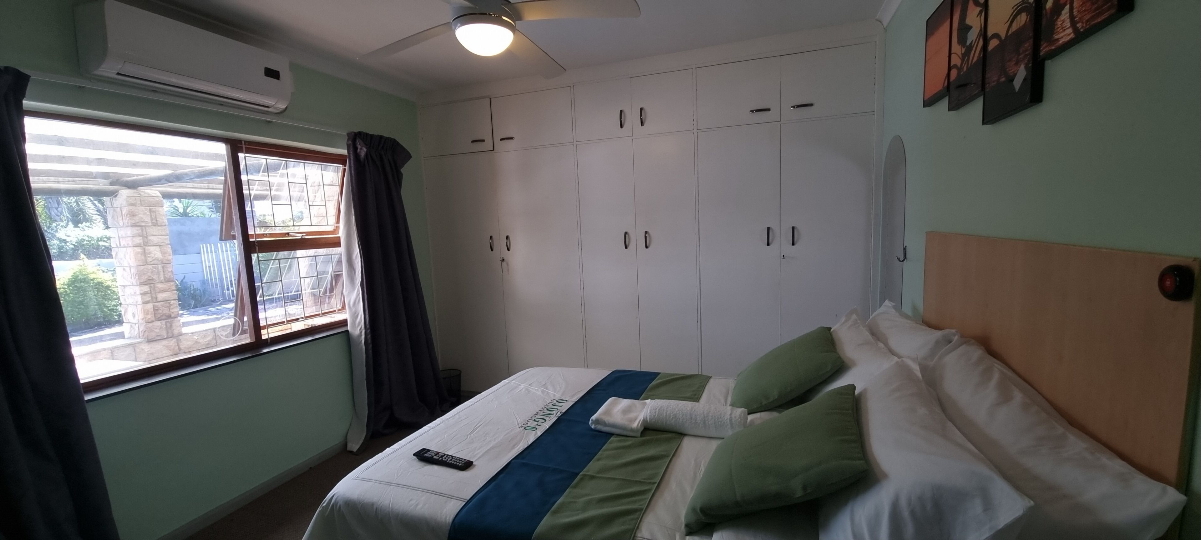 A bedroom with a bed, a ceiling fan, a window with curtains, and a wardrobe.
