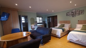 A hotel room with two beds, a sofa, a TV, a desk, and a dining table.