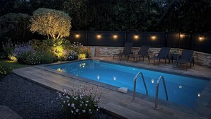 Une piscine avec une terrasse en bois, entourée de chaises et d’un jardin.