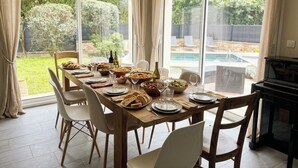 Un coin repas avec une table dressée pour six personnes, un piano et une vue sur une piscine et un jardin.
