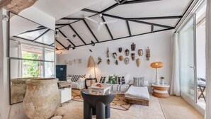 A modern interior with a high ceiling, a large stone pot, a sofa set, and a wall adorned with various masks. - Magnificent 3-bedroom Andalusian family villa near the beach and Puerto Banús (Marbella)