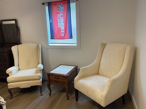 Ein Zimmer mit zwei Sesseln, einem kleinen Holztisch und einem Fenster mit einer Werbetafel.
