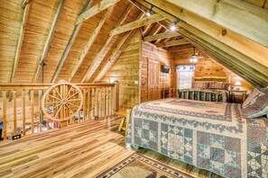 A log cabin bedroom with a wooden ceiling, a bed with a quilt, a wooden rocking chair, and a wooden wheel. - Bear-rif-ic Cabin w/ Hot Tub & Pool Table (Sevierville)