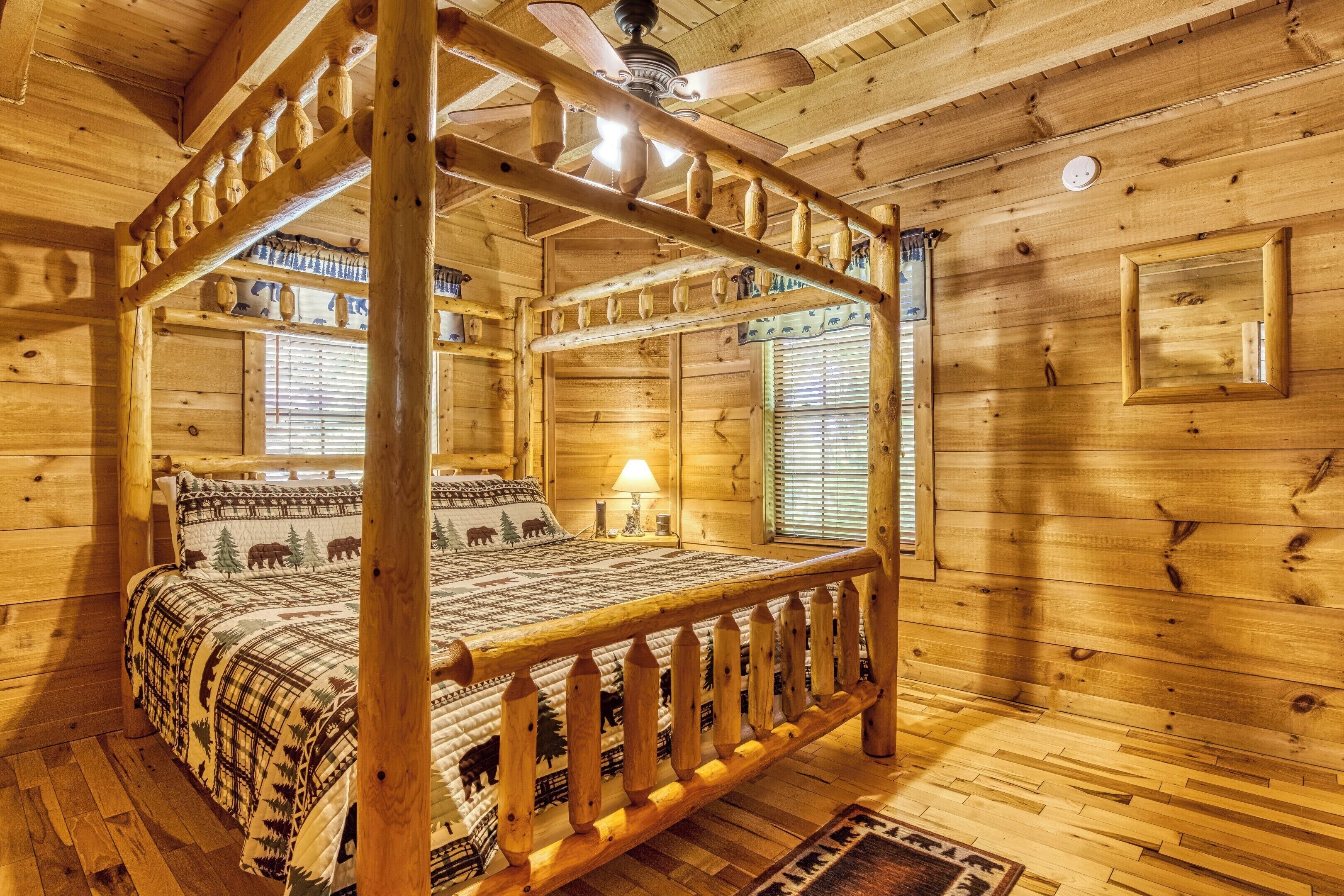 A wooden four-poster bed with a plaid bedspread, a wooden ceiling fan, and a window with blinds.
