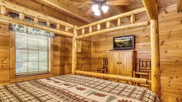 A log cabin room with a bed, a window with blinds, a ceiling fan, and a framed picture on the wall. - Mountain Views & Hot Tub | Near Dollywood (Sevierville)