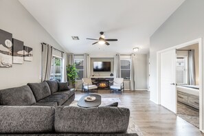 A modern living room with a sectional sofa, a flat-screen TV, a fireplace, and a ceiling fan.