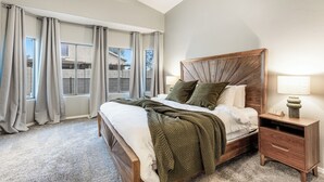 Ein Schlafzimmer mit einem großen Bett, einem Nachttisch mit Lampe und einem Fenster mit Vorhängen.