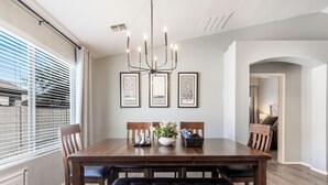 Ein Esszimmer mit Holztisch, Stühlen, einer Bank, einer Chandelüster, gerahmten Kunstwerken und einem Fenster mit Jalousien.