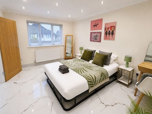 A modern bedroom with a bed, a window with blinds, a mirror, and artwork on the wall. - Spacious & Relaxing 4BR House | Excellent transpo. (Luton)