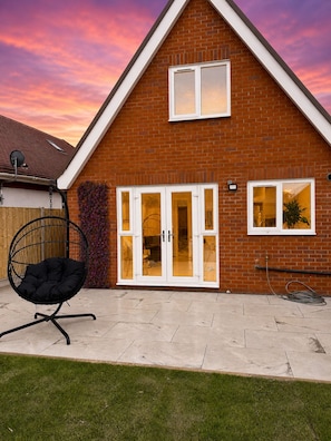A brick house with a tiled patio, a swing chair, and a garden. - Spacious & Relaxing 4BR House | Excellent transpo. (Luton)