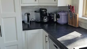 Een keuken met witte kastjes, een koffiezetapparaat, een paarse container en een vaatwasser.