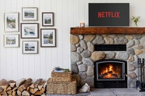 A fireplace with a stone surround, a Netflix sign above it, and framed pictures on the wall. - Otter Lake Cottage, 4 Bedroom, 2 Bath, Lake Views (Seguin)