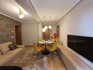 Ett modernt vardagsrum med en soffa, ett matbord, gula stolar, en platt-TV och en mönstrad matta.