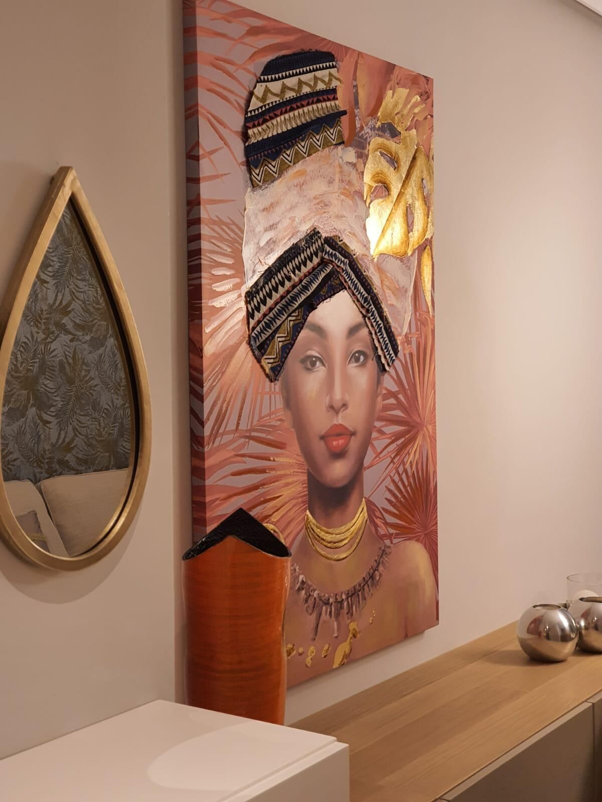 Un mur orné d’un grand tableau, d’un miroir et d’une armoire en bois contenant des objets décoratifs.
