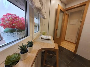 Un pasillo con un banco de madera, una ventana con planta en maceta y una puerta.