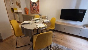 Een eetruimte met een ronde tafel, gele stoelen, een flatscreen-tv en een schilderij aan de muur.