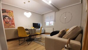 Een woonkamer met een bank, een eethoek met stoelen en een tafel, een televisie en een wandklok.
