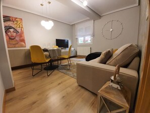 Una sala de estar con sofá, un comedor con sillas y una mesa, un televisor y un reloj de pared.